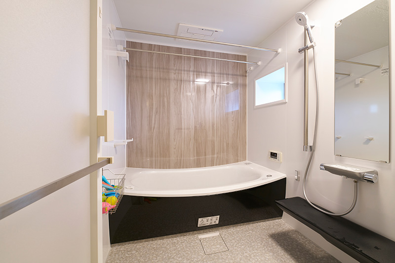 木目調壁と黒い浴槽の落ち着いた浴室