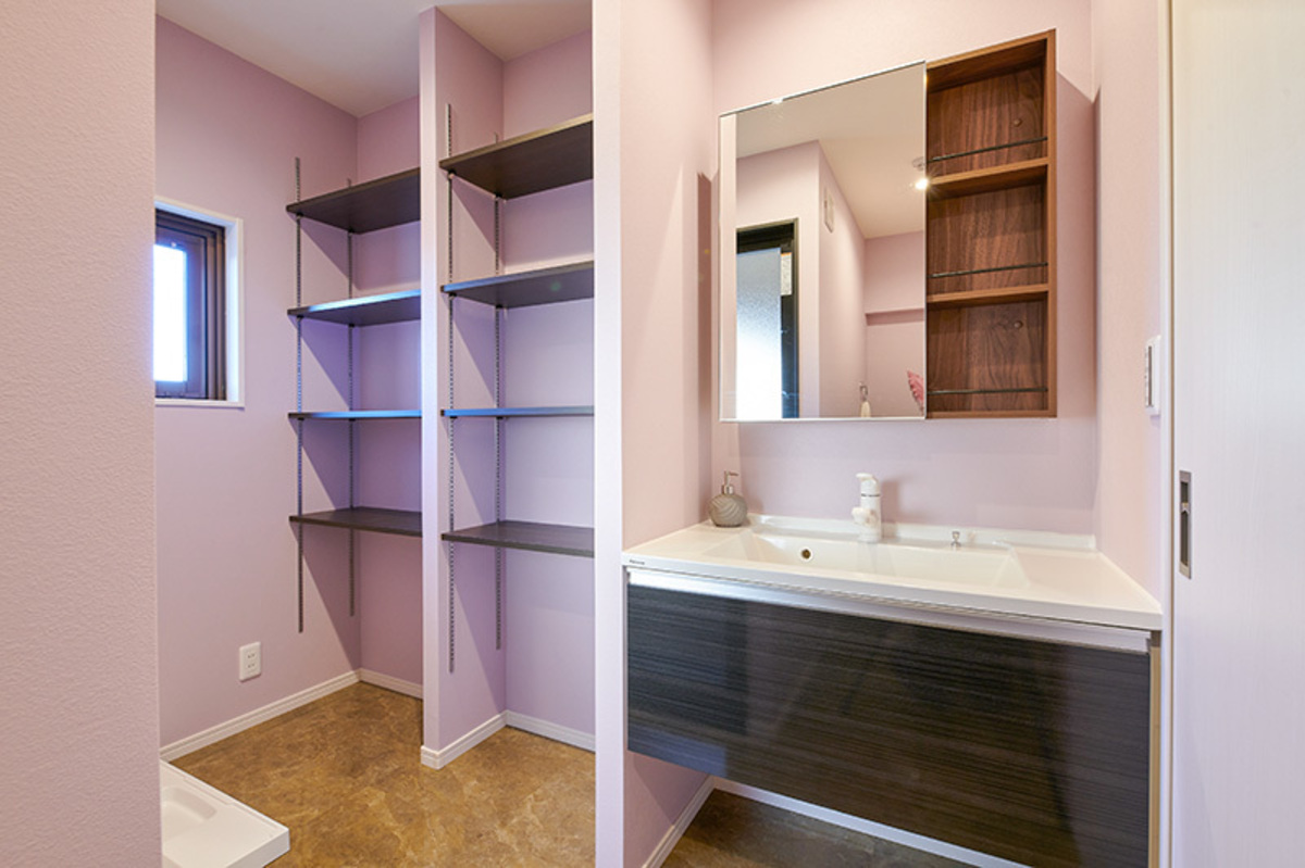 桃色の壁に黒棚が並ぶ広い洗面室